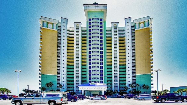 A multi-story hotel with a central tower and symmetrical wings, featuring a parking lot with several vehicles. - Boardwalk Resort 2011 -799987 (Panama City Beach)