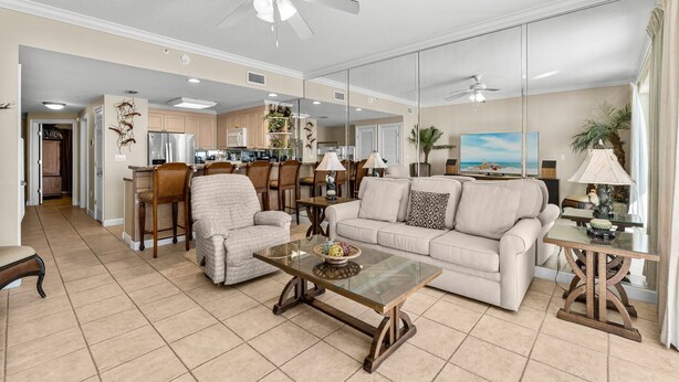 A spacious living room with a glass coffee table, beige sofa, and a dining area with wooden chairs. - Boardwalk Resort 1806 - 556193 (Panama City Beach)