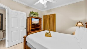 A hotel room with a bed, a ceiling fan, a television on a wooden stand, a curtain, and a bedside table with a lamp. - Boardwalk Resort 1806 - 556193 (Panama City Beach)