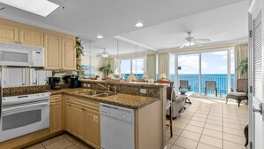 A kitchen with a view of the ocean, a balcony with chairs, and a dining area with a view. - Boardwalk Resort 1806 - 556193 (Panama City Beach)