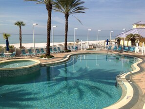 A clear swimming pool with a wavy edge, surrounded by lounge chairs and palm trees. - Boardwalk Resort 511 (Panama City Beach)