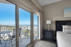 A hotel room with a balcony, a bed, a nightstand, and a view of the beach. - Beach Manor @ Tops'l 705 (Miramar Beach)