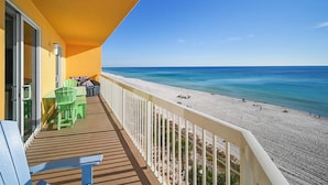 Un balcon avec vue sur la plage, une table avec des chaises et un petit coin salon.