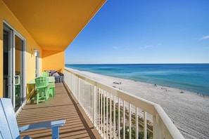 Un balcon avec vue sur la plage, une table avec des chaises et un petit coin salon.