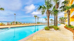 Une piscine à l’eau d’un bleu cristallin, entourée de palmiers et bordée d’un sentier menant à un bâtiment aux murs jaunes.