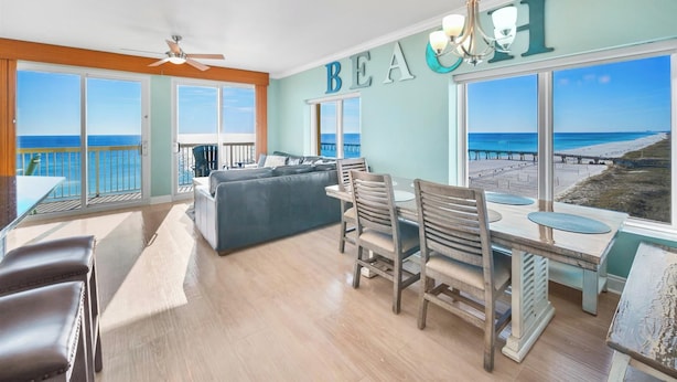 Un vaste espace de vie comprenant un grand canapé, une table à manger et des chaises, avec vue sur une plage et une jetée.