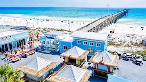 Un hôtel situé en bord de mer, doté de bâtiments à toits de chaume, d’une jetée s’avançant dans l’océan et d’une plage de sable.