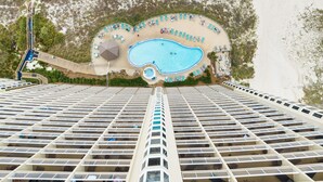 A high-rise hotel with a rooftop pool, multiple balconies, and a beach area with sun loungers. - Emerald Beach 1525 (Panama City Beach)