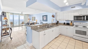 A modern kitchen with white cabinets, a granite countertop, and a built-in oven. - Emerald Beach 1525 (Panama City Beach)