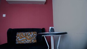 A room with a black sofa, a patterned pillow, a small white table, and a white shelf against a red wall. - VAKANA STUDIO'S 202-One space, everything at the right place (Nairobi)
