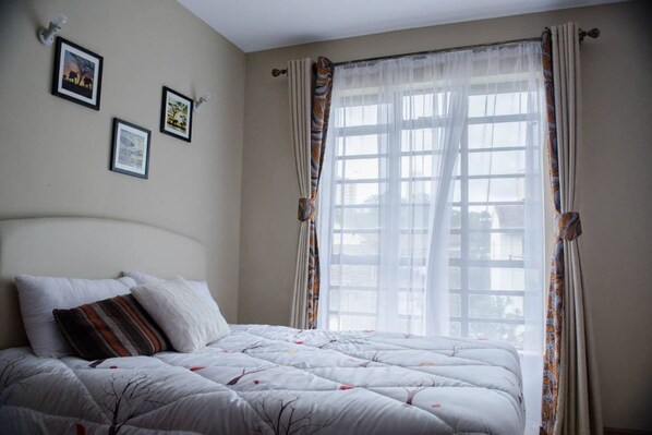A bedroom with a bed, a window with curtains, and three framed pictures on the wall.