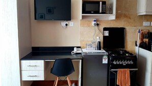 A compact kitchen with a microwave, stove, and a small refrigerator. There is a flat-screen TV mounted on the wall and a chair in front of a desk. - VAKANA STUDIO'S 202-One space, everything at the right place (Nairobi)