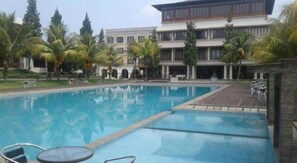A swimming pool with lounge chairs and a building with multiple floors and balconies.