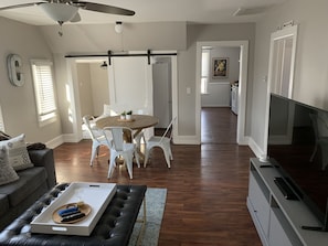 Una sala moderna con comedor, televisor y cocina al fondo.
