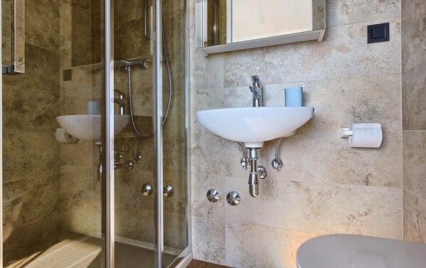 A bathroom with a glass shower enclosure, a white sink with a mirror above it, and a toilet.