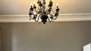 Un salón con un sofá gris, una mesa de centro negra, un jarrón rosa con flores y una araña negra.