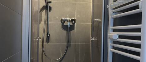 A modern shower stall with a glass door, a handheld showerhead, and a wall-mounted faucet.
