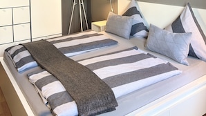 Un dormitorio moderno con una cama grande, una mesita de noche, una lámpara de pie y un armario.