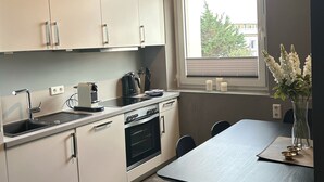 Una cocina moderna con armarios blancos, horno empotrado y ventana con vistas a zonas verdes.