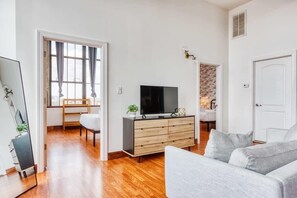 A modern living room with a flat-screen TV, a grey sofa, wooden flooring, and a white door.