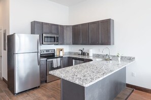 A modern kitchen with dark cabinets, stainless steel appliances, and a granite countertop. - Sosuite | 2BR Penthouse w W/D, Gym, On-Site Bar (Philadelphia)