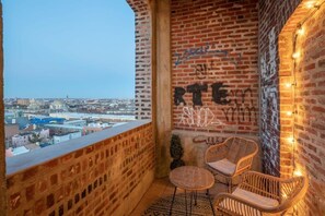 A balcony with brick walls, two wicker chairs, and a view of the cityscape.