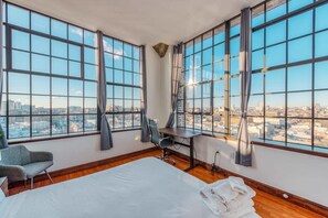 Una habitación de hotel con ventanas amplias, una cama, un escritorio y una silla.