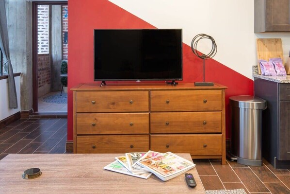 Una habitación con un aparador de madera, un televisor encima y un cubo de basura a la derecha.