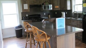 A kitchen with wooden cabinets, a central island with bar stools, a microwave, and a coffee maker.