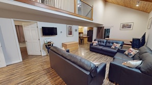 A spacious living area with a large sofa set, a flat-screen TV, and a wooden floor.