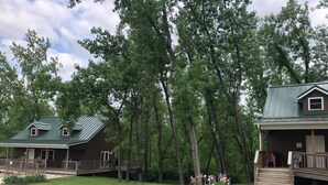 A cabin with a porch and a covered deck area, surrounded by trees and a grassy yard.