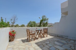 An outdoor patio with stone flooring, a table with chairs, and a potted plant with red flowers. - Casa Verde di Naxos (Naxos)