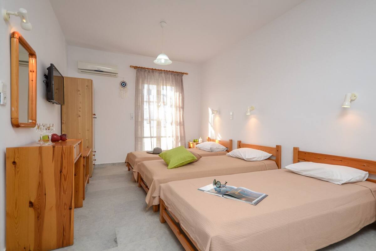 A hotel room with two beds, a wooden dresser, a TV, and a window with curtains.