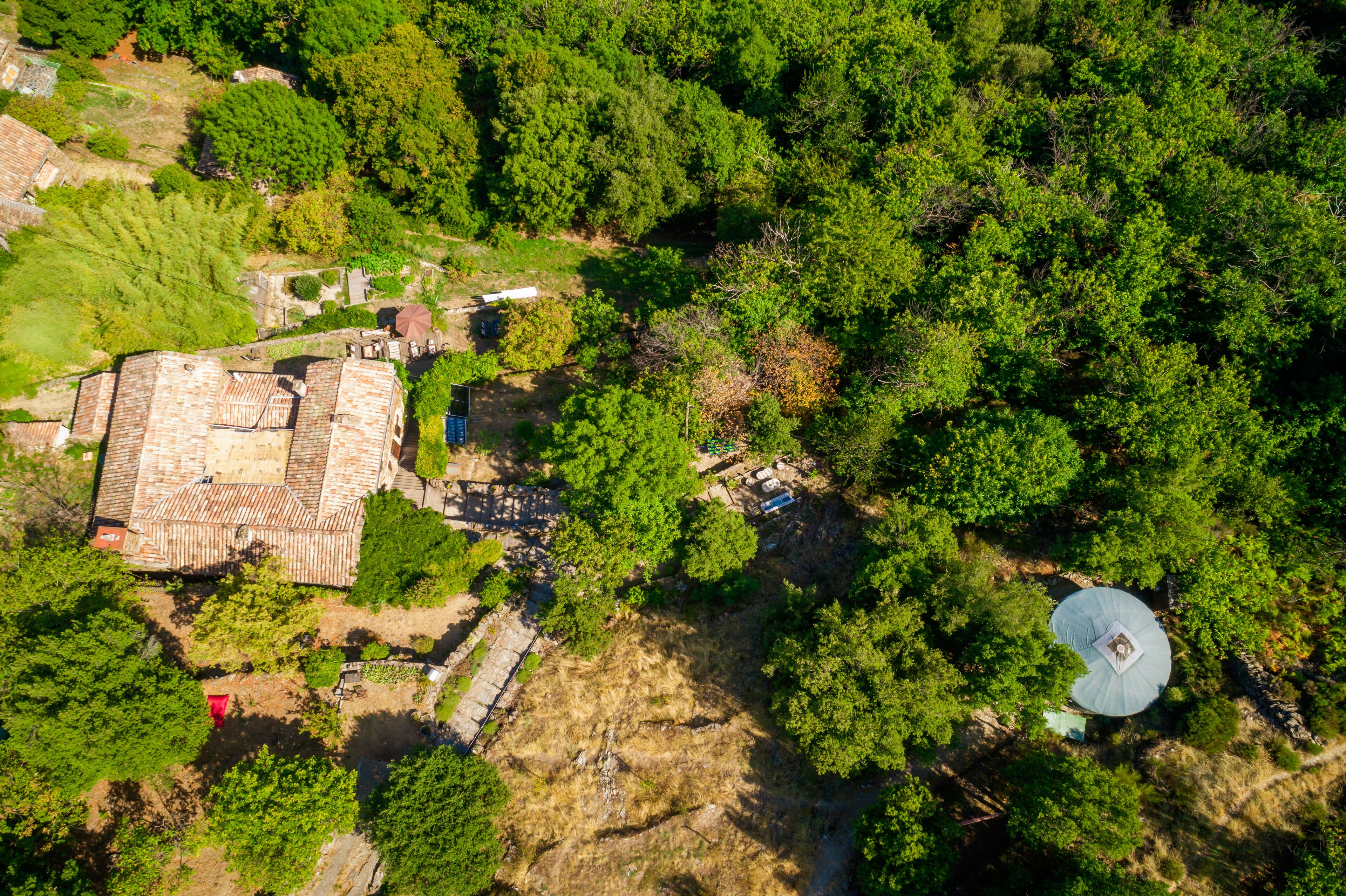 Luchtbeeld van een pand met een groot gebouw, een kleinere constructie en dichte bebossing.