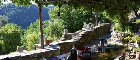 Un área de comedor al aire libre con muros de piedra y plantas en macetas, con vistas a un paisaje montañoso.
