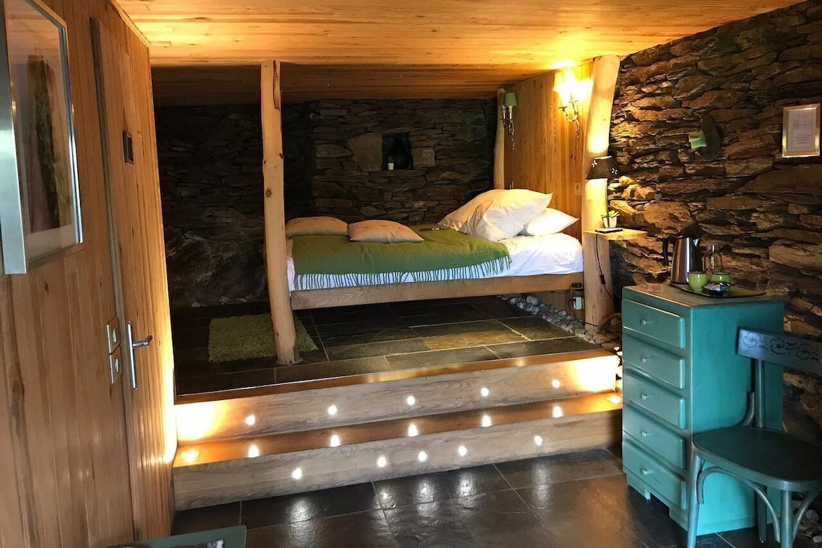 A cozy cabin-style room with a bunk bed, stone walls, wooden ceiling, and a teal dresser.