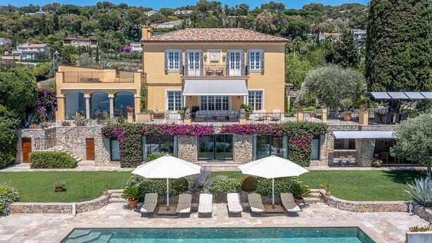 Une grande maison à deux étages, dotée d’une piscine, d’un espace salon extérieur et d’un jardin.