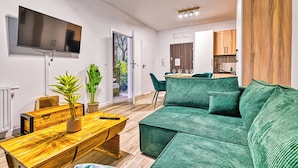 Un salon moderne avec un canapé vert, une table basse en bois et un téléviseur fixé au mur.