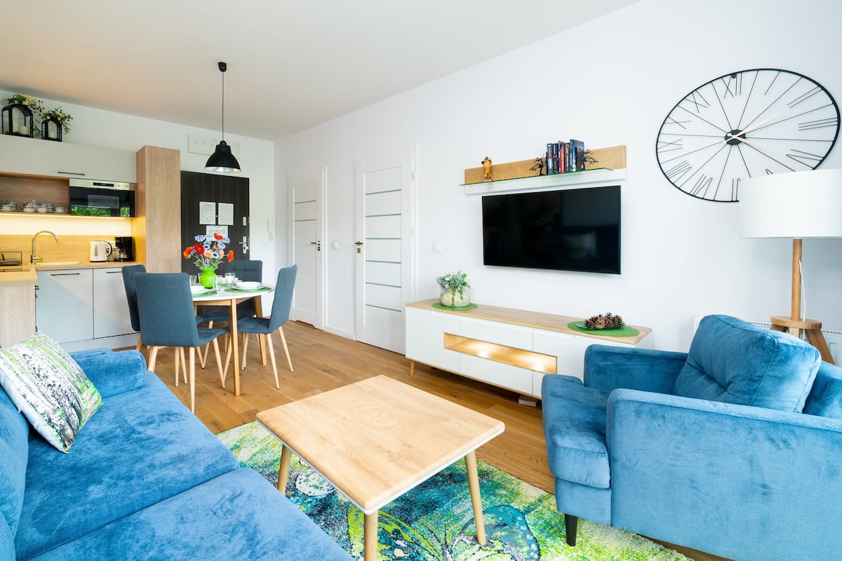 Ein modernes Wohnzimmer mit einem blauen Sofa, einem Holztisch und einem an der Wand befestigten Fernseher.