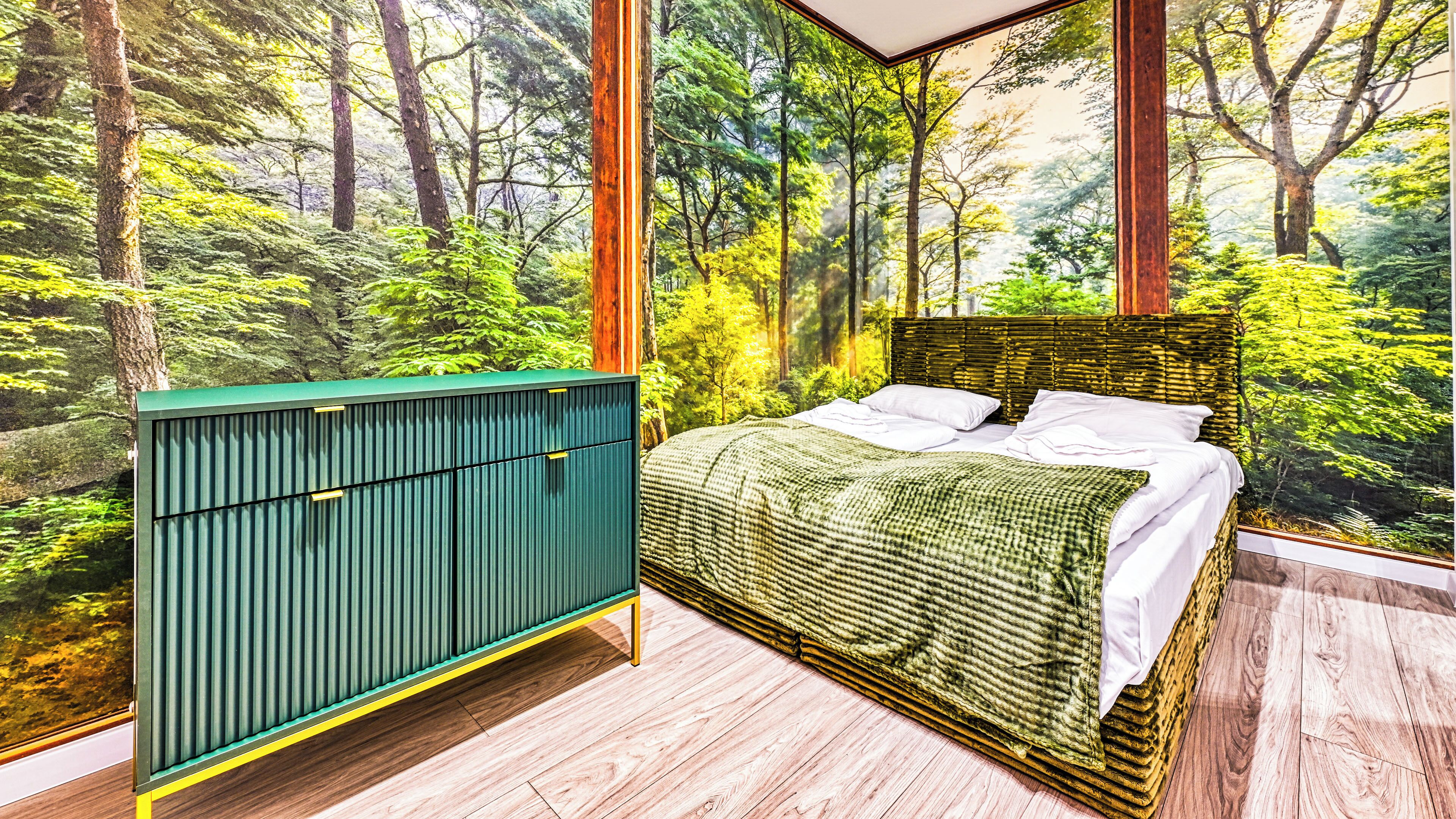 Un dormitorio con cama, un radiador y un ventanal con vistas al bosque.