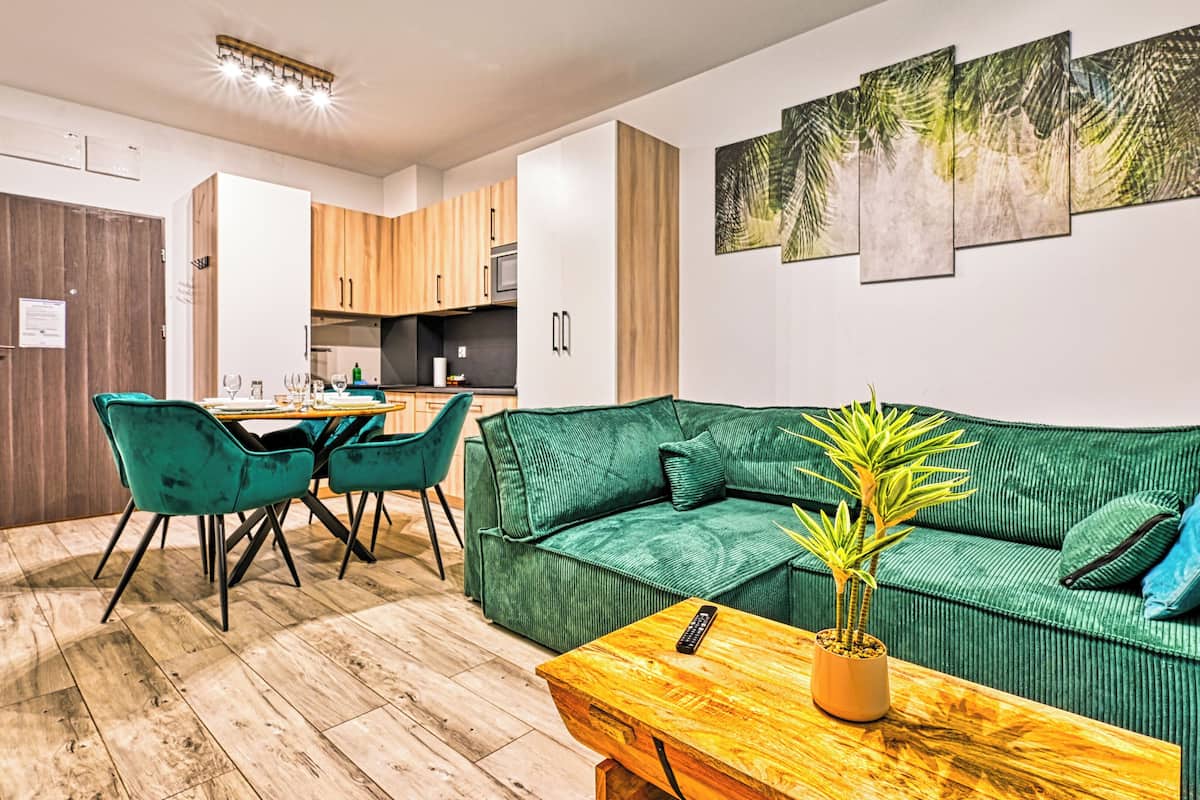 Ein modernes Wohnzimmer mit einem grünen Sofa, passenden Sesseln, einem Holztisch und einer Topfpflanze.