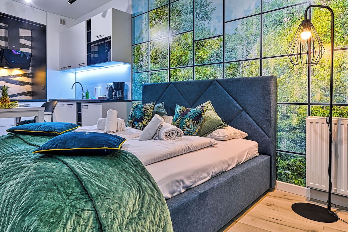 Ein modernes Schlafzimmer mit einem großen Bett, einem Schreibtisch und Blick auf Grün durch ein Fenster.
