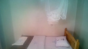 A single bed with a wooden frame, white bedding, and a mosquito net. - Nyeri Star Rest And Lodge (Nyeri)