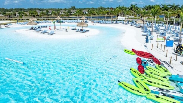 A beach resort with a clear blue pool, lounge chairs, and kayaks.