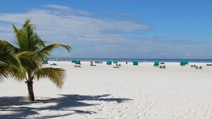 A beach with white sand, palm trees, and green beach umbrellas.
