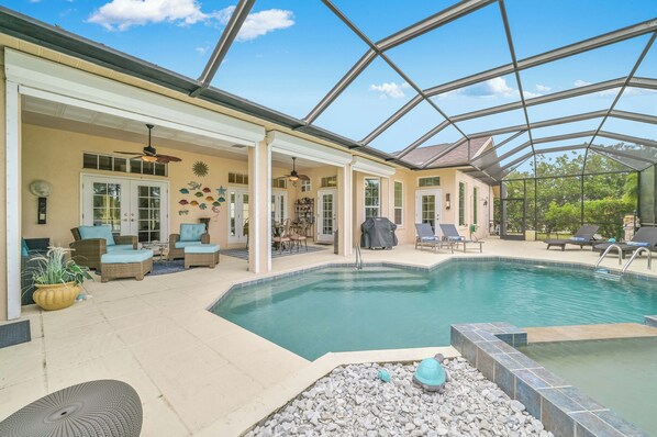 A covered outdoor pool area with lounge chairs and a patio table.