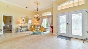 A spacious living room with a dining area, a chandelier, and large windows with decorative glass panels.