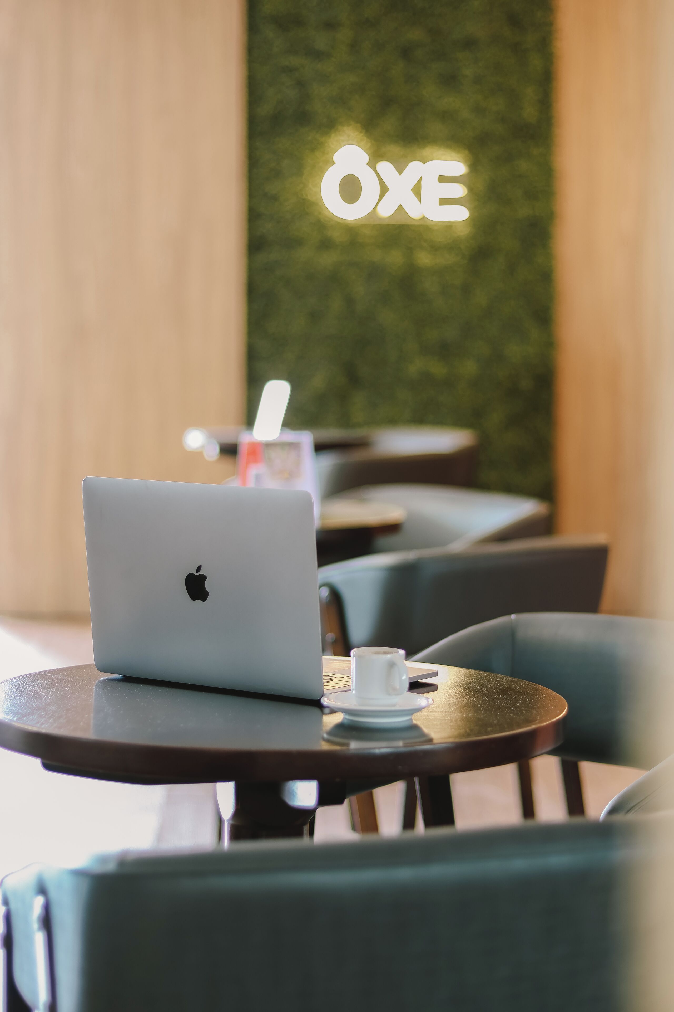A café with a laptop on a table, a cup, and a green wall with a sign.