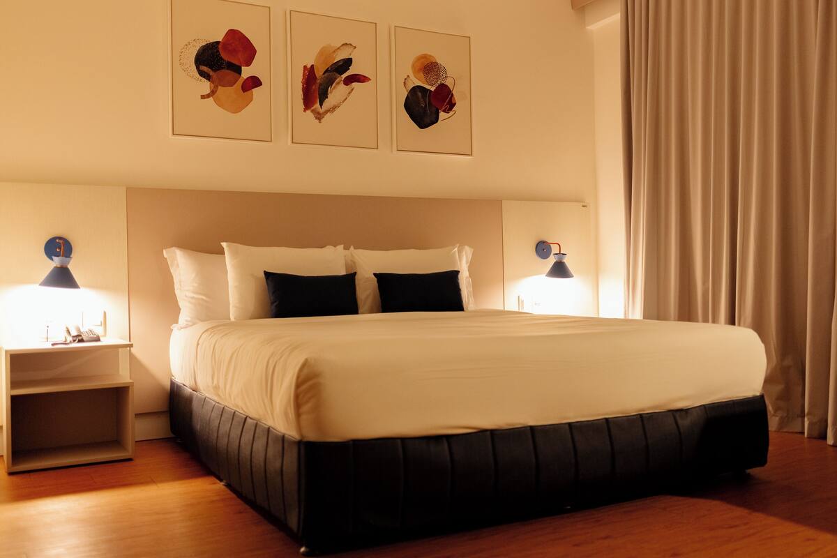 A neatly made bed with white and black bedding, two bedside lamps, and a nightstand with a phone and a small plant.