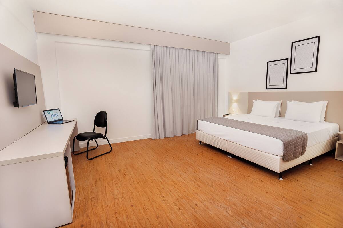 A hotel room with a bed, desk, chair, and a TV.